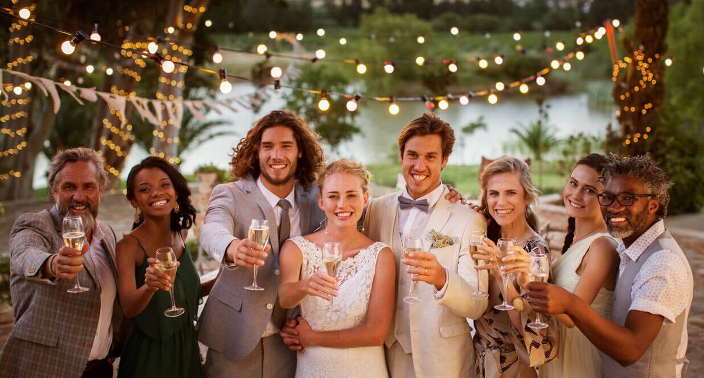 Group of smiling wedding guests toasting with champagne flutes at an outdoor reception